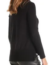 Buzo de punto color beige con cuello volcado amplio, mangas largas acanaladas y torso liso. Presenta una costura central vertical, ruedo con tajos laterales y largo asimétrico, siendo más largo en la parte posterior.