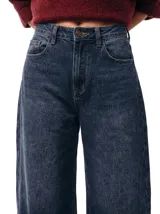 Jean de tiro alto con silueta barrel, caracterizado por su pierna amplia con una leve forma curva. Confeccionado en denim de color azul profundo con un sutil efecto lavado, presenta un diseño de cinco bolsillos y cierre frontal con botón y cremallera.