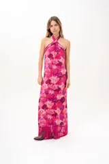 Vestido largo fucsia con estampado abstracto en tonos rosados y morados, cuello halter cruzado y flecos largos en el dobladillo inferior.