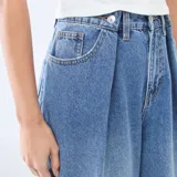 Jean de corte wide leg y tiro alto, confeccionado en denim azul. Presenta pinzas en la cintura, cierre frontal con botón y bolsillos laterales.