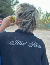 Camisa negra de manga corta con cuello, confeccionada en tejido texturizado (tipo waffle o piqué). Presenta un bordado en la espalda con el texto "Ittai Stars" en hilo blanco.