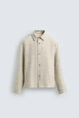 Sobrecamisa de hombre de corte relajado, color beige claro con textura jaspeada en tonos claros y oscuros. Presenta cuello solapa, manga larga con puño abotonado y cierre frontal de botonadura.