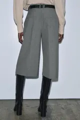 Bermuda larga gris confeccionada en hilatura con viscosa, de tiro medio y cintura con trabillas. Presenta bolsillos laterales ocultos en costura, detalle de raya plancha y cierre frontal con cremallera, botón y ganchos metálicos.