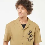 Camisa de manga corta color beige con cuello cubano y bordado de flores en el pecho.