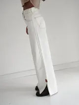 Pantalón vaquero de tiro alto y corte recto, color blanco, con aberturas laterales en los bajos y detalles de terminación en cuero.