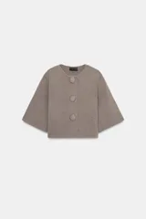 Chaqueta corta de punto color beige, con cuello redondo y manga tres cuartos. Cierre frontal con tres botones forrados a tono.