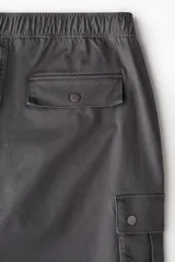 Pantalon cargo gris oscuro de corte holgado y diseño amplio, confeccionado en tejido de algodón. Cuenta con cintura elastizada con botón a presión, bolsillos laterales al bies y bolsillos cargo con solapa y botones a presión en las piernas.