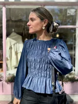 Blusa de denim azul con diseño fruncido elástico en todo el cuerpo, mangas largas abullonadas con puños elásticos y ruedo con volado.