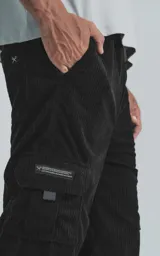 Pantalón cargo de pana negra, corte ancho y tiro alto con elástico en la cintura. Presenta bolsillos cargo amplios a los lados de las piernas, uno de ellos con un pequeño detalle de etiqueta o cierre.