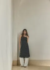 Top largo de tejido satinado color negro con estampado de lunares blancos, diseño recto, tirantes finos y ribetes de encaje negro en el escote y el ruedo.