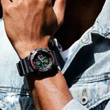 Reloj analógico-digital Casio G-Shock con caja y malla de resina negra. Presenta una esfera robusta con detalles en rojo y naranja, resistencia a impactos y al agua hasta 200 metros.