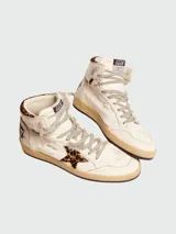 Championes de caña alta Golden Goose modelo Sky-Star, confeccionados en cuero color blanco con efecto desgastado. Presentan detalles en piel de poni con estampado de leopardo en la estrella lateral y el cuello. Incluyen cordones grises y etiqueta GGDB en la lengüeta.