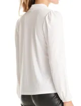 Blusa de seda fría color negro, con escote en V y lazo decorativo al cuello. Presenta mangas largas abullonadas con puños elásticos y detalles de strass aplicados en cuello, lazo y mangas.