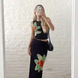 Conjunto de dos piezas compuesto por un top sin mangas y una pollera larga, confeccionados en microtul negro con estampado floral en tonos verdes y rojos. El top es ajustado y la pollera presenta un diseño de doble capa con cintura elástica.