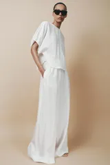 Pantalón palazzo color blanco, confeccionado en tejido de lyocell, de tiro medio, cintura elástica ajustable con cordones, bolsillos laterales ocultos y pierna ancha.