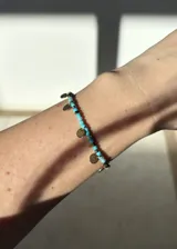Pulsera de acero inoxidable con baño de oro PVD 18k, con cuentas de color turquesa y dijes circulares dorados.