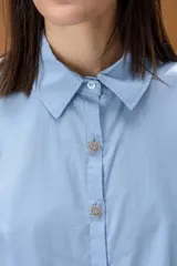 Camisa de manga larga en color celeste, con cuello clásico y cierre frontal de botones decorativos con forma de estrella brillante.