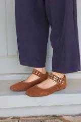 Ballerina de gamuza color marrón, con tira ajustable en el empeine que incluye hebilla metálica y detalles de ojales plateados.