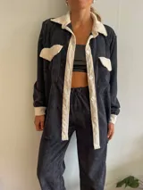 Camisa de pana negra con cuello, solapa, botones y bolsillos de parche en color crema. Corte recto y mangas largas.