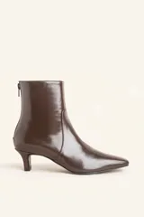 Bota de caña corta confeccionada en cuero vacuno color chocolate con acabado brillante. Presenta punta fina, cierre posterior y taco chupete bajo.