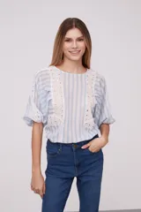 Blusa blanca con rayas verticales celestes, mangas abullonadas y detalles de calado en los hombros y el frente.