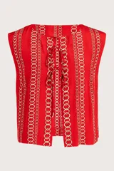 Chaleco sin mangas de color rojo con estampado de cadenas doradas en disposición vertical. Presenta escote redondo y cierre frontal mediante cordones entrelazados.