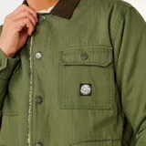 Campera de estilo utilitario color verde oliva, con forro interno de corderito y cuello de pana marrón. Presenta cierre frontal con botones, dos bolsillos superiores con solapa y bolsillos laterales. Incluye etiqueta tejida en el pecho.