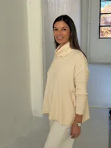 Polerón de punto color crudo con cuello alto tipo polera, mangas largas con puños acanalados y diseño holgado con aberturas laterales.