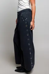 Pantalon de tiro bajo y pierna ancha confeccionado en denim negro con efecto vintage, decorado con ojales metálicos a lo largo de los laterales y los bolsillos.