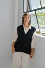Chaleco de punto negro con escote en V profundo y diseño de trenzas verticales en el frente. Presenta un corte holgado y terminaciones en tejido acanalado.
