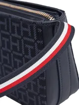 Cartera tipo bandolera de Tommy Hilfiger, confeccionada en poliuretano con patrón jacquard de monogramas en tonos azul marino. Presenta cierre superior con cremallera y detalles distintivos de la marca en los laterales.