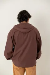 Canguro marrón con capucha, confeccionado con un panel frontal de gamuza en un tono más oscuro y cierre frontal parcial. Presenta puños elásticos y un bolsillo frontal tipo canguro.