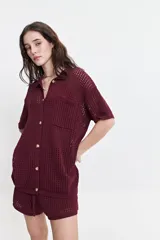 Camisa tejida color borgoña con textura calada, cuello clásico, botones y mangas cortas con elástico.