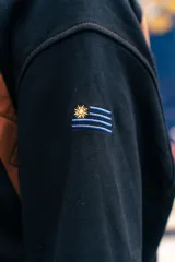 Buzo amarillo de corte holgado con mangas raglán en color azul, detalle de costuras acolchadas en los hombros y bordado de sol en el centro del pecho. Presenta puños y cuello acanalados con rayas azules.