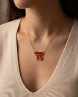 Collar de acero con baño de oro y dije en forma del símbolo Jai esmaltado en rojo, con cadena fina de eslabones.