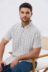 Camisa de manga corta confeccionada en mezcla de lino y algodón, con diseño a cuadros en tonos gris, blanco y azul. Presenta cuello camisero con botones y bolsillo ojal en el pecho con detalle bordado.
