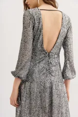 Vestido corto de fiesta con lentejuelas plateadas en patrón de espiga, mangas tres cuartos y cuello redondo. El diseño presenta un ajuste entallado con un cinturón ancho negro de gamuza con hebilla metálica dorada en forma de corazón.