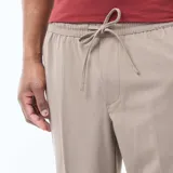 Pantalón de corte jogger en color beige, confeccionado con cintura elástica ajustable mediante cordón y bolsillos laterales.