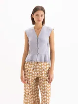 Top Selene al cuerpo de color gris, con escote en V, sin mangas con volados en la sisa y cierre frontal con ganchos niquelados decorativos. Cuenta con un diseño de dobladillo con volados en la parte inferior.