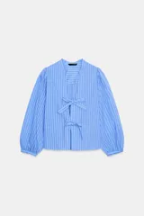 Camisa celeste a rayas verticales, con escote en pico, mangas largas abullonadas con puños elásticos y cierre frontal con lazos del mismo tejido.