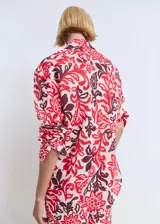 Camisa de corte recto y diseño holgado, confeccionada en algodón con estampado floral en tonos rojos y bordó sobre fondo crudo. Presenta cuello camisero clásico, cierre frontal con botones y mangas largas.