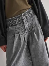 Pantalón wide leg de tiro medio confeccionado en denim blanco. Presenta una cintura con diseño de pasacintas entrelazadas, cierre frontal y bolsillos laterales. Su diseño de pierna amplia ofrece una caída fluida con volumen.