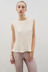 Top sin mangas de tela plisada en color beige, con cuello bote y corte recto con caída fluida.