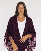 Ruana tejida en lana merino de color bordó, con flecos decorativos en tonos bordó y rosado en los bordes.