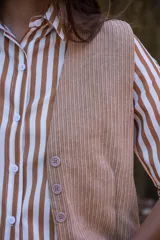 Camisa de corte clásico con estampado de rayas verticales en tonos blanco y marrón. Presenta cuello camisero, cierre frontal con botones y mangas largas con puños rectos. Confeccionada en tela liviana con caída suave.