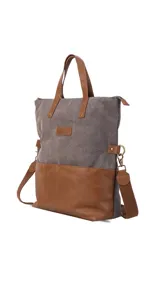 Cartera tipo tote bag combinada en tela canvas gris y detalles en cuero sintético color suela. Cuenta con doble asa de mano, correa larga ajustable y extraíble, cierre superior y bolsillo frontal. Incluye compartimento interno para notebook.