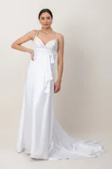 Vestido largo de novia blanco con corte imperio y tirantes finos. Presenta el cuerpo superior bordado a mano con abalorios y pedrería, faja drapeada con lazo lateral y falda fluida con cola.