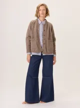 Saco de lana color marrón, de tejido grueso, con cuello redondo y botones frontales. Presenta mangas raglán con detalle de punto acanalado y bolsillos delanteros tipo parche.