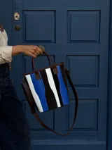 Matera de cuero con diseño de paneles verticales en combinación de colores azul, verde, marrón y bordó. Cuenta con dos asas cortas de cuero y estructura rígida.