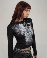 Remera de manga larga con capucha integrada, color negro con estampado gráfico frontal en blanco. La capucha presenta detalles de ojales metálicos decorativos.